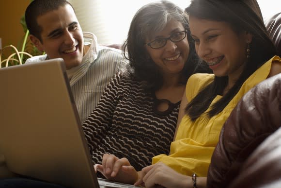 Mom and children sitting on couch laughing with daughter using laptop.