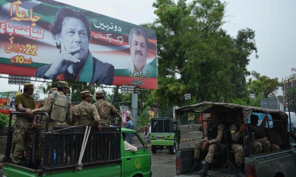 Pakistani soldiers in Rawalpindi patrol on a street beside a billboard featuring an image of Pakistani cricketer turned politician Imran Khan.