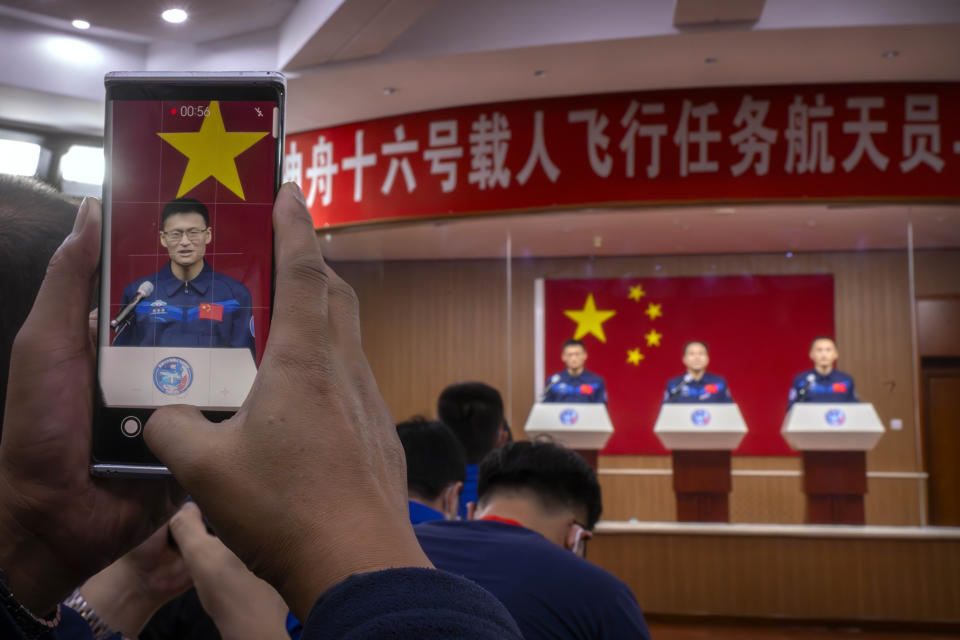 A staff member takes a smartphone photo of Gui Haichao, a Chinese astronaut as he stands behind glass during a meeting with the press at the Jiuquan Satellite Launch Center in northwest China on Monday, May 29, 2023. China's space program plans to land astronauts on the moon before 2030, a top official with the country's space program said Monday. (AP Photo/Mark Schiefelbein)