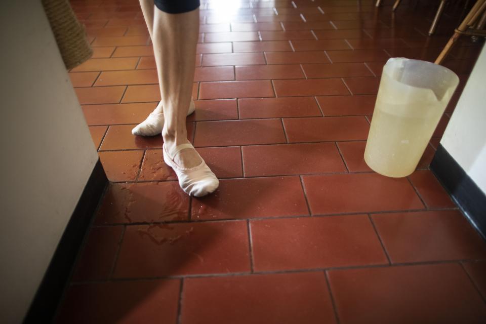 Carolina Wolf, bailarina del Ballet Teresa Carreño, se moja las zapatillas para no resbalar mientras entrena en la sala de su casa en Caracas durante la cuarentena por la pandemia del coronavirus, el martes 11 de agosto del 2020. (AP Foto/Ariana Cubillos)