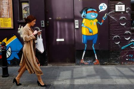 FILE PHOTO - A woman looks at her mobile phone as she passes a mural in Shoreditch, London, Britain October 5, 2016. REUTERS/Stefan Wermuth