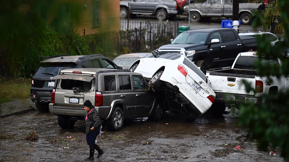 A woman walks by cars damaged by floods during a rainstorm in San Diego on Monday, January 22, 2024. - Denis Poroy/AP