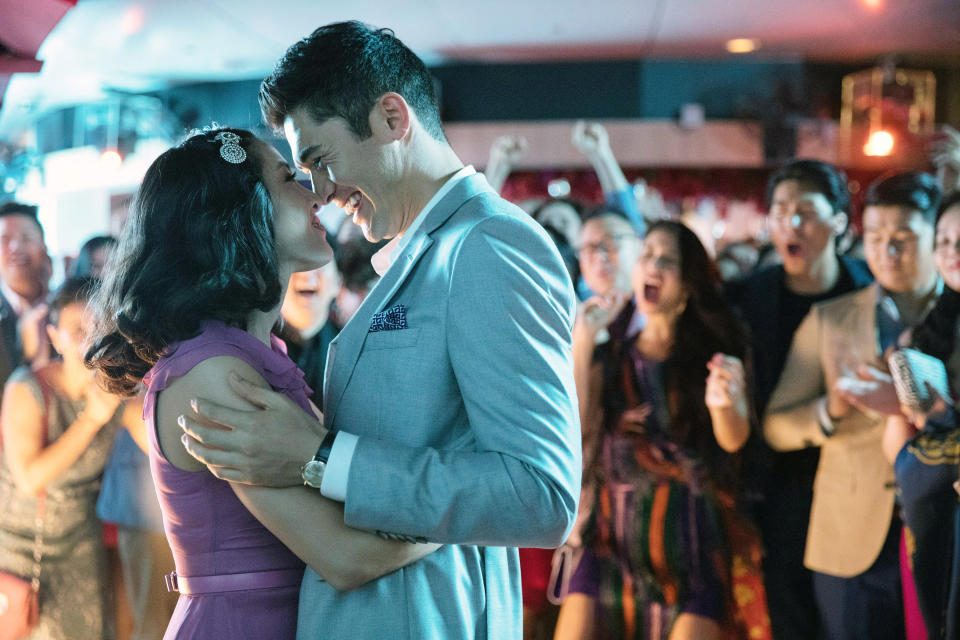 Constance Wu and Henry Golding share a joyful embrace in a crowded, festive atmosphere, with people cheering in the background