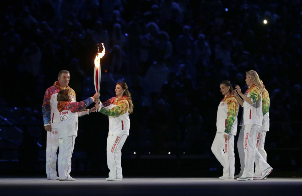 Irina Rodnina, left, receives the torch from Alina Kabaeva as Vladislav Tretyak looks at them, during the opening ceremony of the 2014 Winter Olympics in Sochi, Russia, Friday, Feb. 7, 2014. (AP Photo/Matt Dunham)