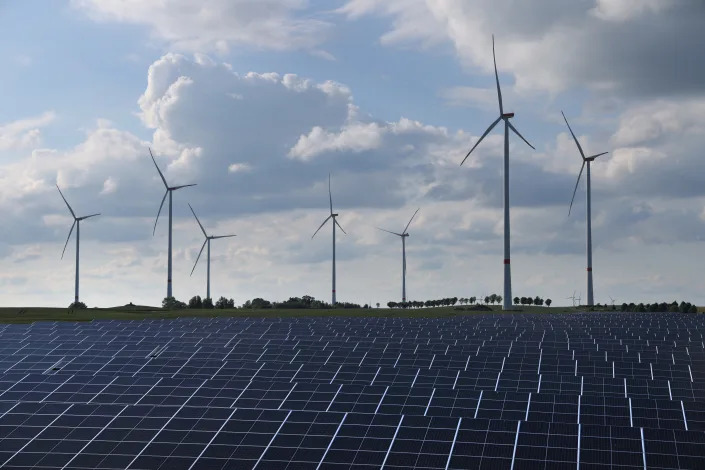 Wind turbines spin behind a vast array of solar energy panels.