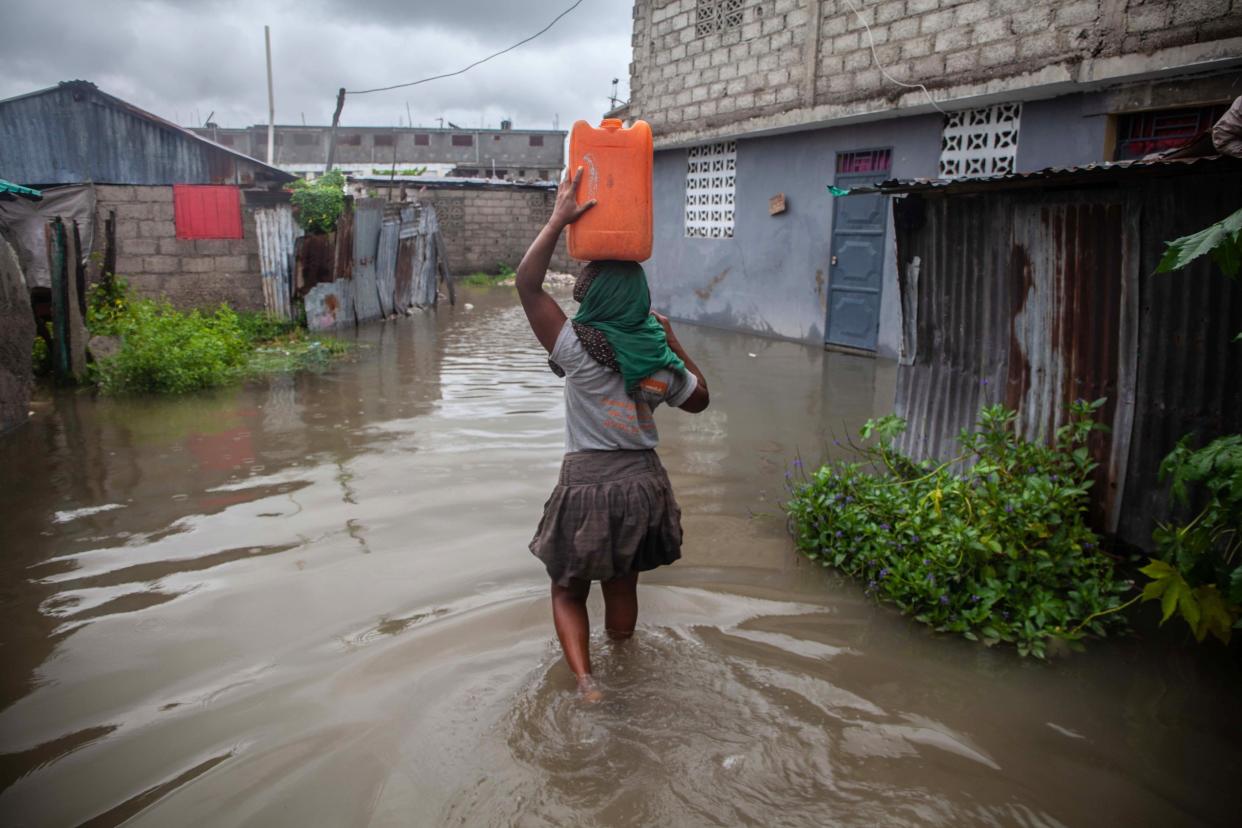 A woman carries a jerrycan on her head through a flooded area as heavy rain brought by tropical storm Grace hits Haitians just after a 7.2-magnitude earthquake struck Haiti on Aug. 17, 2021, in Les Cayes, Haiti.