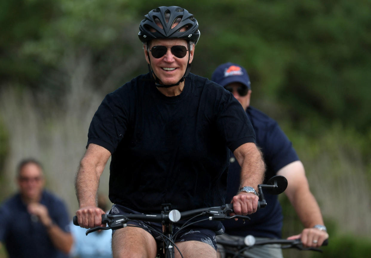 President Biden, looking jubilant in bicycle helmet, pedals ahead.