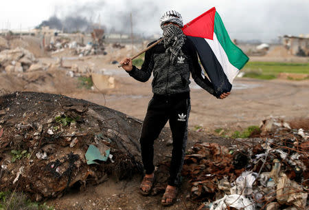 A protester holds a Palestinian flag as he poses for a photograph at the scene of clashes with Israeli troops near the border with Israel, east of Gaza City, January 19, 2018. "The battle between us and the Israeli occupation has been ongoing for decades. We will continue to protest and resist as long as there is one Israeli occupier on our land. Trump and anyone else in this world will not be able to control our anger," he said. REUTERS/Mohammed Salem