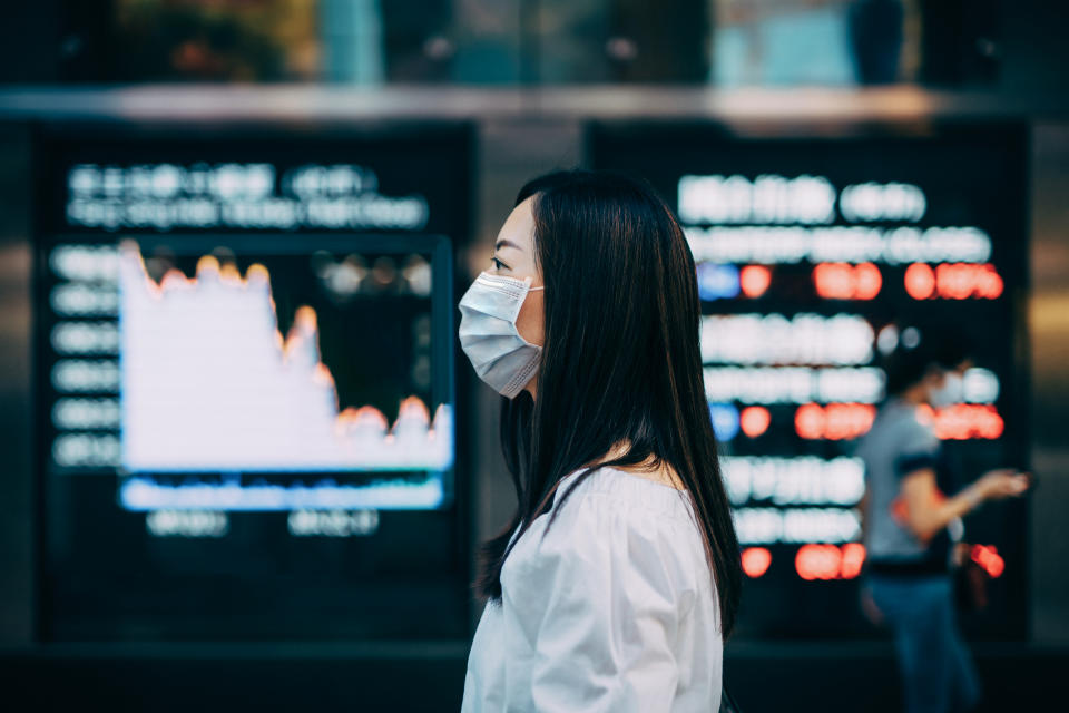 Businesswoman with protective face mask standing in front of stock exchange market display screen