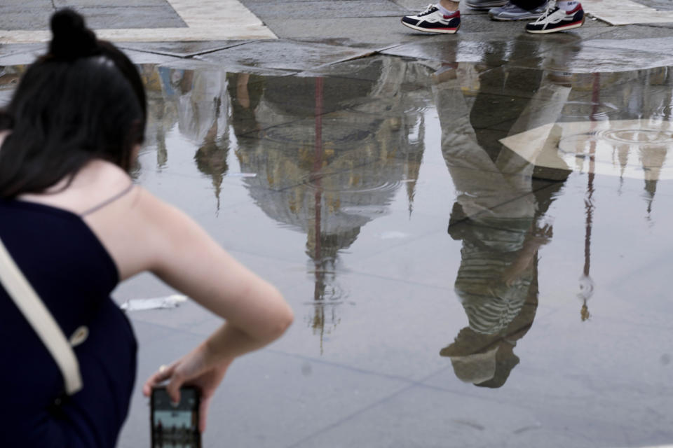 Tourists are reflected in a puddle, in St Mark's square, Venice, Italy, Wednesday, Sept. 13, 2023. The Italian city of Venice has been struggling to manage an onslaught of tourists in the budget travel era. The stakes for the fragile lagoon city are high this week as a UNESCO committee decides whether to insert Venice on its list of endangered sites. (AP Photo/Luca Bruno)