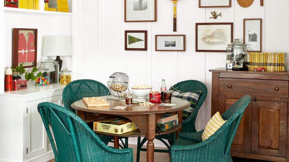 tavern table, green painted rattan chairs, gallery wall of family photos and vintage rackets and paddles in game room of a lakeside cabin in houston lake, georgia