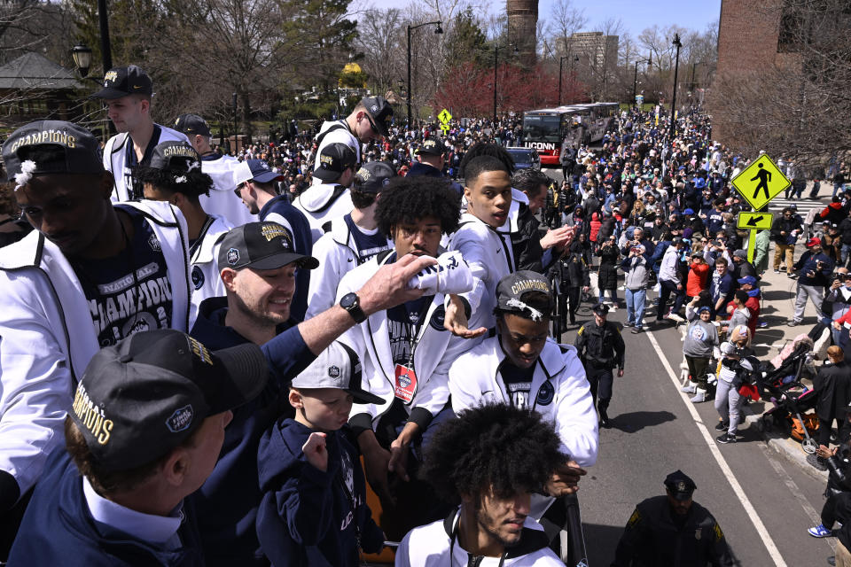 Connecticut Gov. Ned Lamont, left, hands a T-shirt for UConn's Jordan Hawkins to toss during a parade to celebrate the team's NCAA college basketball championship, Saturday, April 8, 2023, in Hartford, Conn. (AP Photo/Jessica Hill)