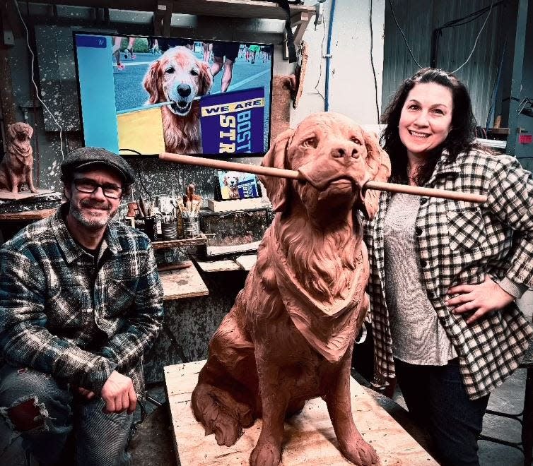 Sculptor Jeff Buccacio, left, and his wife, Nina, pose with the sculpture of Spencer, a therapy dog from Holliston that became famous for supporting runners on the Boston Marathon route. The sculpture is being installed at 11 Frankland Road in Ashland, which is near where Spencer, who died in 2023, used to stand.