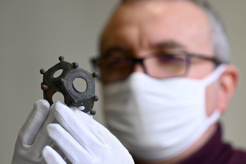 A person wearing a mask and white gloves holding a metal dodecahedron