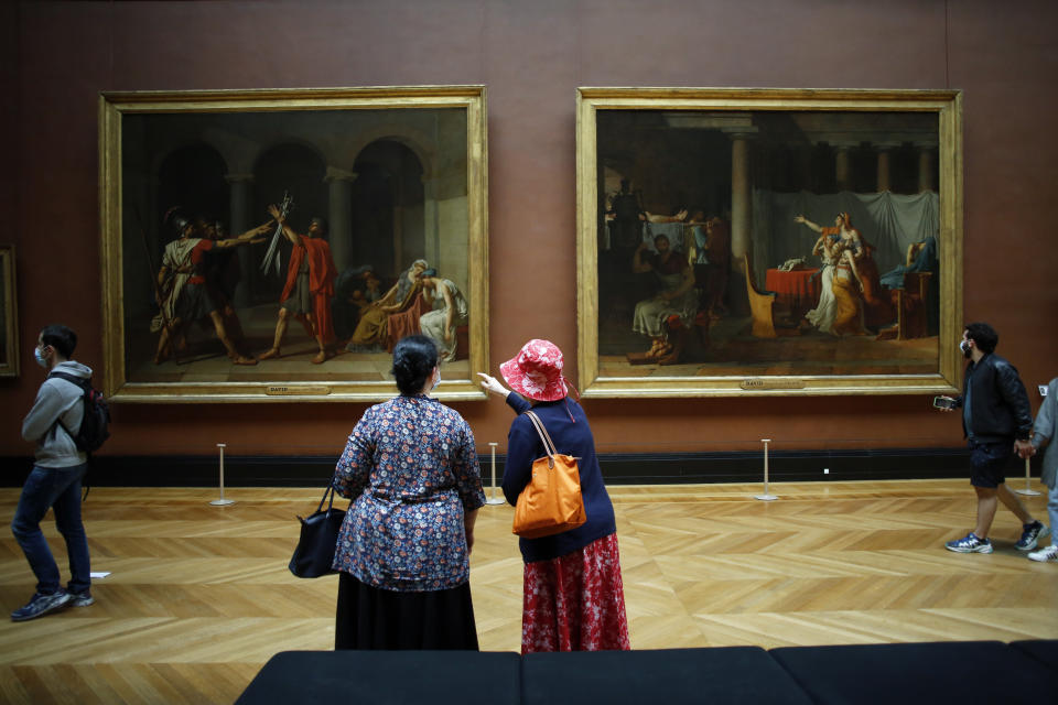 Visitors watch oil on canvas entitled Le serment des Horaces, left, and Licteurs rapportant à Brutus le corps de ses fils, by Jacques Louis David in the Louvre Museum, in Paris, Monday, July 6, 2020. The home of the world's most famous portrait, the Louvre Museum in Paris, reopened Monday after a four-month coronavirus lockdown. (AP Photo/ Thibault Camus)