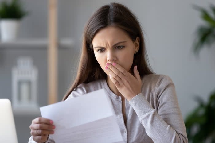 A woman holds her hand over her mouth in surprise at a bill.