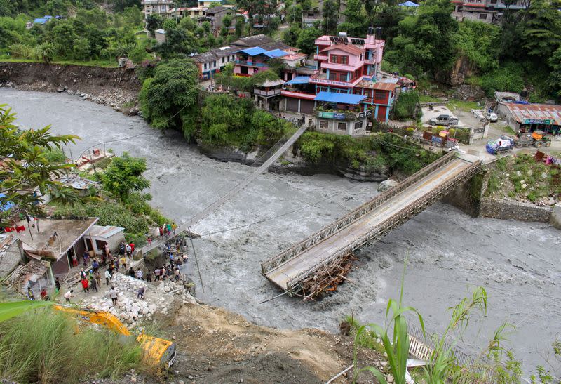 People gather near the bridge that is damaged due to the flood at Raghu Ganga River in Myagdi