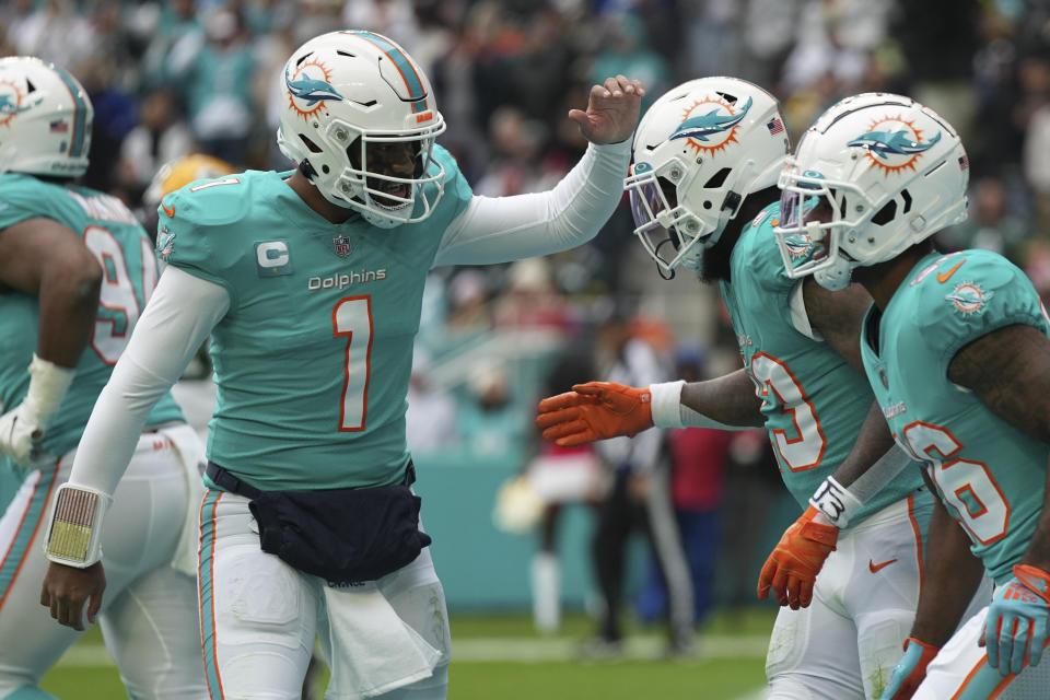 Miami Dolphins quarterback Tua Tagovailoa (1) congratulates Miami Dolphins running back Jeff Wilson Jr. (23), center, after he scored a touchdown during the first half of an NFL football game against the Green Bay Packers, Sunday, Dec. 25, 2022, in Miami Gardens, Fla. (AP Photo/Jim Rassol)