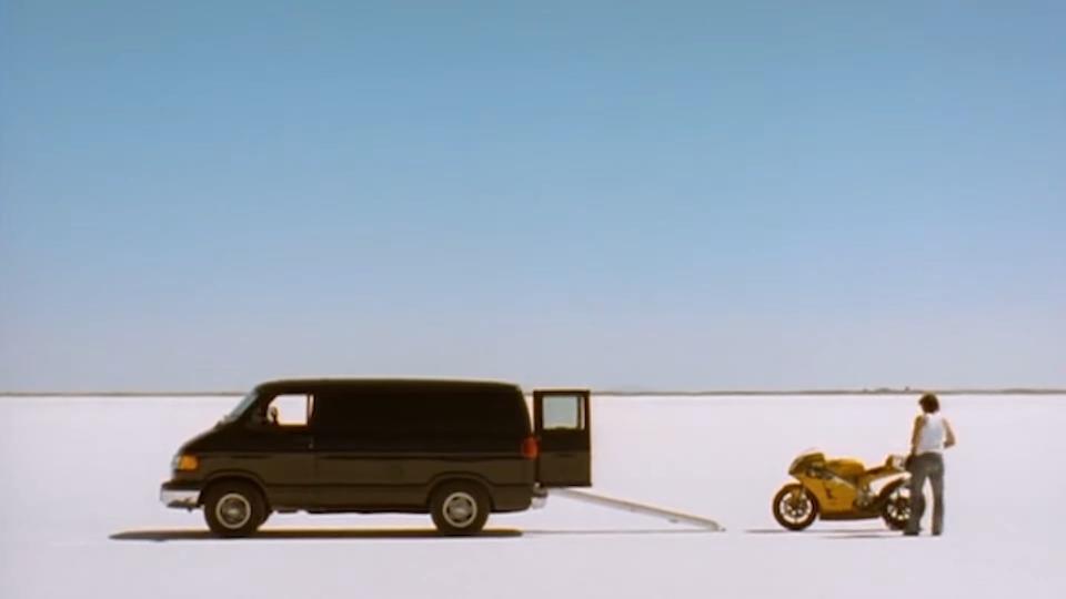 Bud standing by his motorcycle with an open van next to him in "The Brown Bunny"