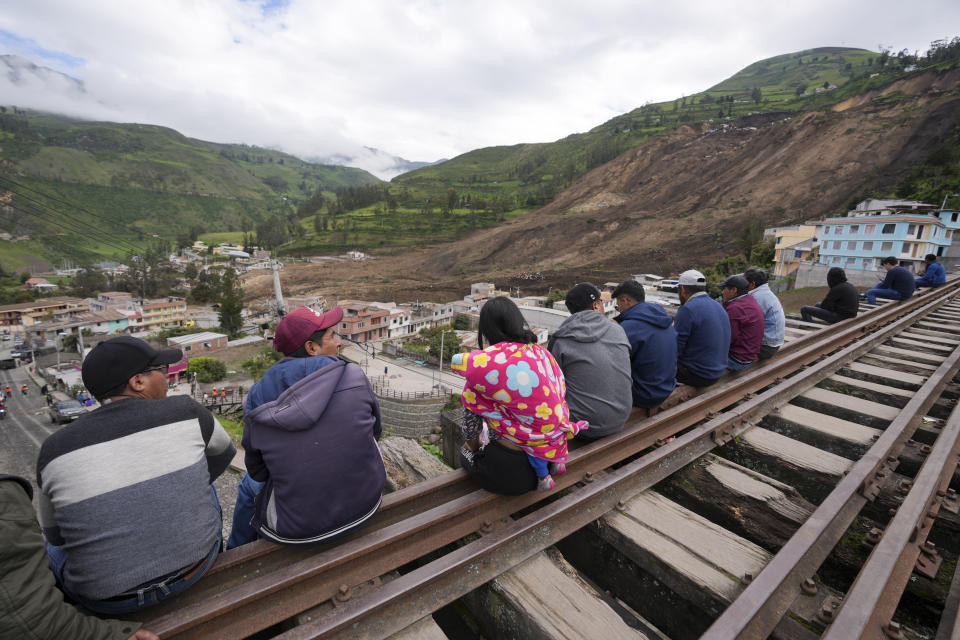 Residents sit on rail tracks overlooking a landslide that swept over Alausi, Ecuador, Tuesday, March 28, 2023, a day after an avalanche buried dozens of homes killing at least seven people. (AP Photo/Dolores Ochoa)