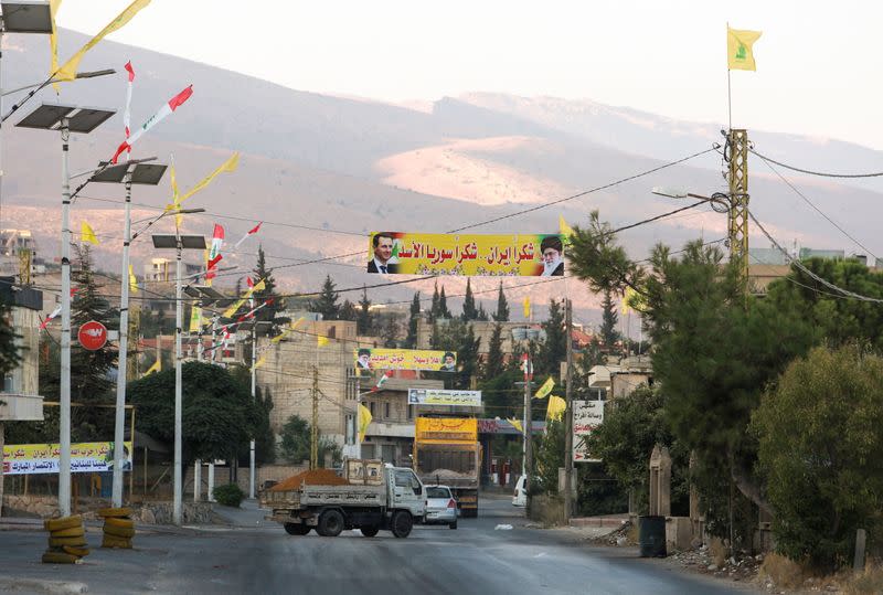 Vehicles ride near a banner depicting Syria's President Bashar al-Assad, and Iran's Supreme Leader Ayatollah Ali Khamenei as the first truck carrying Iranian fuel is expected to reach Lebanon today, near the Lebanese-Syrian border, in al-Ain village