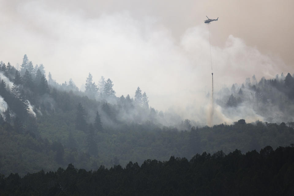 This photo taken Aug. 6, 2018, shows a helicopter dumping water on a section of the Coal Hollow Fire near U.S. Highway 6. An Idaho prisoner sent to help fight a wildfire in Utah raped a woman who also was working to support firefighters, prosecutors said Tuesday, Sept. 4, 2018. The woman had rejected several advances from Ruben Hernandez, 27, in the days before the Aug. 29 assault at the base camp, Sanpete County attorney Kevin Daniels said. Hernandez has been charged with felony rape. (Evan Cobb/The Daily Herald via AP)