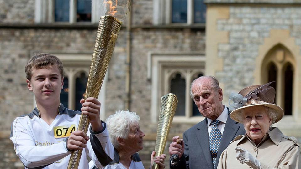 Queen Elizabeth II and Prince Philip, Duke of Edinburgh look on as Olympic torch bearer Gina Macgregor hands the flame to Phil Wells at Windsor Castle on day 53 of the London 2012 Olympic Torch Relay on July 10, 2012 in Windsor, England