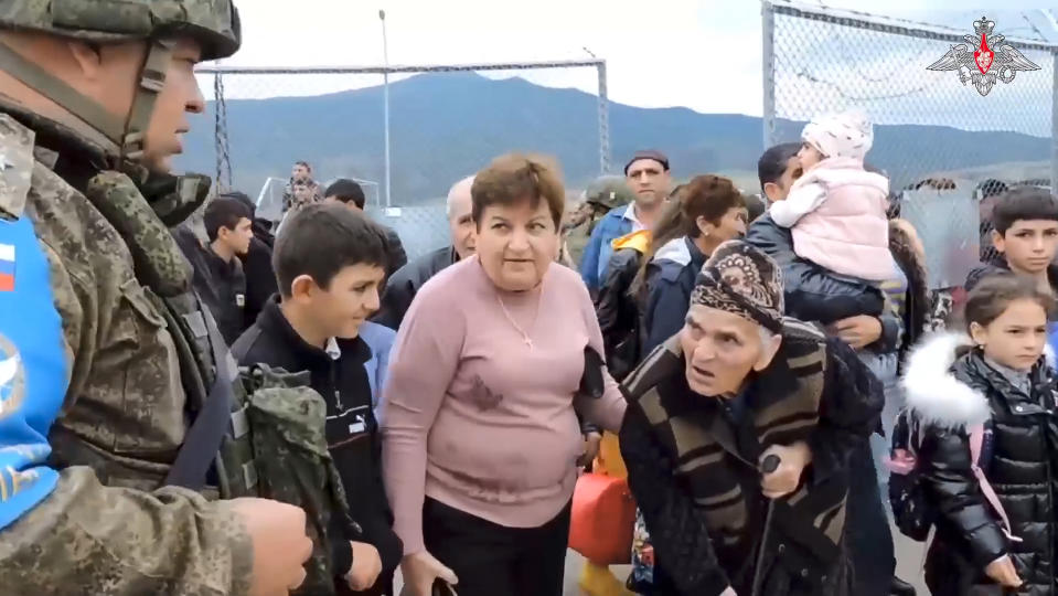 In this image made from video released by Russian Defense Ministry Press Service on Thursday, Sept. 21, 2023, a Russian peacekeeper speaks to ethnic Armenians as they walk through a gate into a camp near Stepanakert in Nagorno-Karabakh. Thousands of Nagorno-Karabakh residents flocked to a camp operated by Russian peacekeepers to avoid the fighting, while many others gathered at the airport of the regional capital, Stepanakert, hoping to flee the region. (Russian Defense Ministry Press Service via AP)