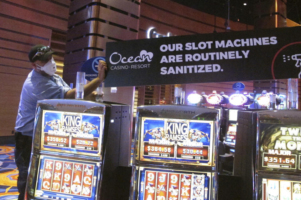 This June 3, 2020, photo shows a worker at the Ocean Casino Resort in Atlantic City, N.J., installing a sign indicating that slot machines will routinely be sanitized once the casino reopened a month later to prevent the spread of the coronavirus. On Jan. 24, 2024, the New Jersey Supreme Court rejected an attempt by the casino to collect on a business interruption policy for the 3 1/2 months it was closed due to the pandemic. (AP Photo/Wayne Parry)