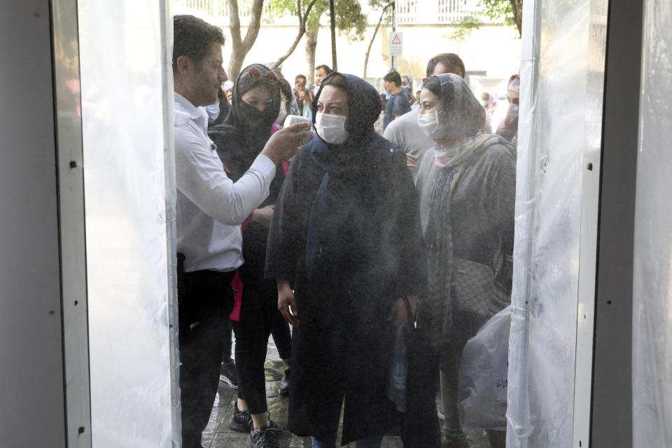 In this Wednesday, June 10, 2020, photo, people have their temperature checked as they enter a disinfectant tunnel to help prevent the spread of the coronavirus at the entrance of a shopping center at the Tehran's Grand Bazaar, Iran. As businesses open and people begin to move around more, health experts fear a growing complacency among Iran’s 80 million people may further allow the virus to spread. (AP Photo/Vahid Salemi)