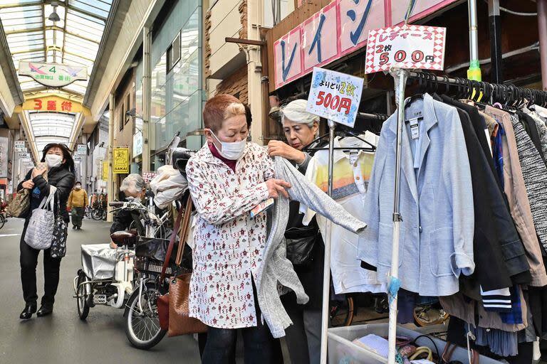 Esta foto tomada el 15 de marzo de 2024 muestra a compradores con barbijo probándose ropa de segunda mano a la venta en una calle comercial de Osaka.