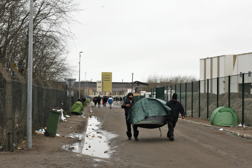 Migrants carry a tent in a makeshift camp, in Calais, northern France, on Friday, Jan.31, 2020. Britain officially leaves the European Union on Friday. (AP Photo/Thibault Camus)