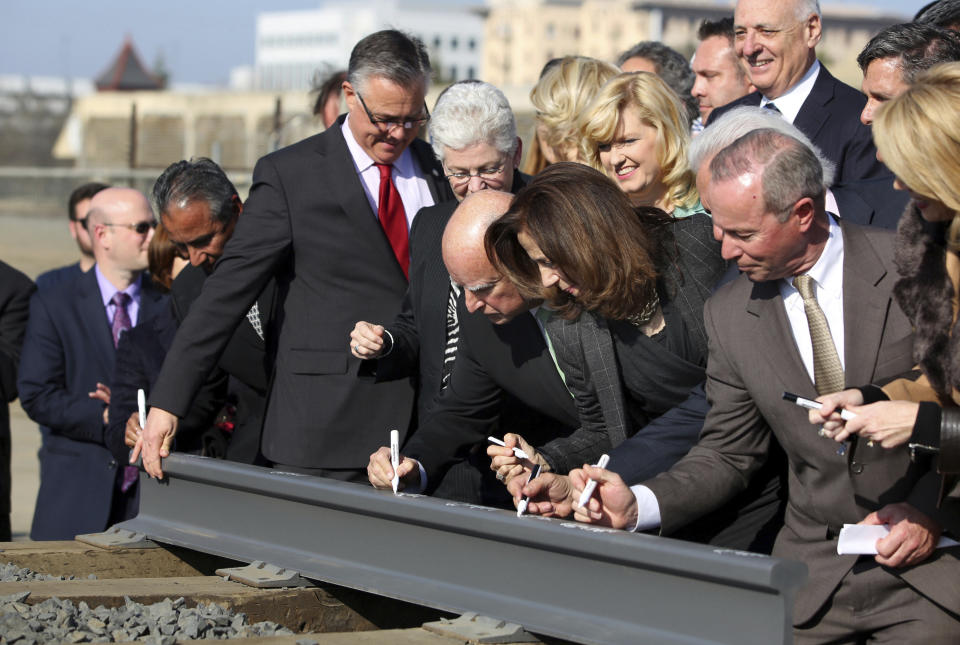 FILE - In this June. 18, 2015 file photo, Gov. Jerry Brown, center, and his wife, Anne Gust Brown, fourth from right, sign a portion of a rail at the California High-Speed Rail Authority in Fresno, Calif. Lawmakers and the Newsom administration are still trying to reach agreement on whether to give the project $4.2 billion that's left in the bond fund voters approved for high-speed rail in 2008. Rail officials say the need it to continue construction beyond next summer, but some state lawmakers want more oversight of the project before releasing it. (AP Photo/Gary Kazanjian, File)