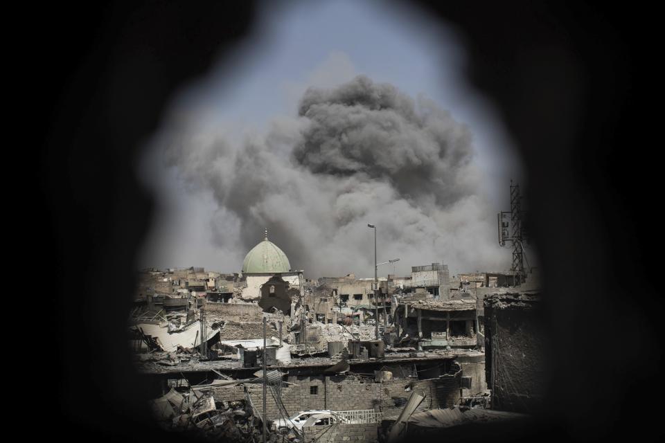 FILE - A bomb explodes behind the al-Nuri mosque complex, as seen through a hole in the wall of a house, as Iraqi Special Forces move toward Islamic State militant positions in the Old City of Mosul, Iraq, June 29, 2017. (AP Photo/Felipe Dana, File)
