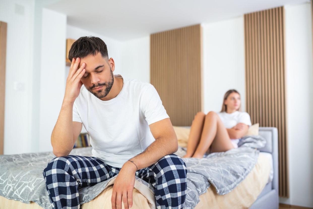 Beautiful girl and a frustrated man sitting in bed and not looking at each other. Upset couple ignoring each other. Worried man in tension at bed. Young couple angry with each other after a fight.