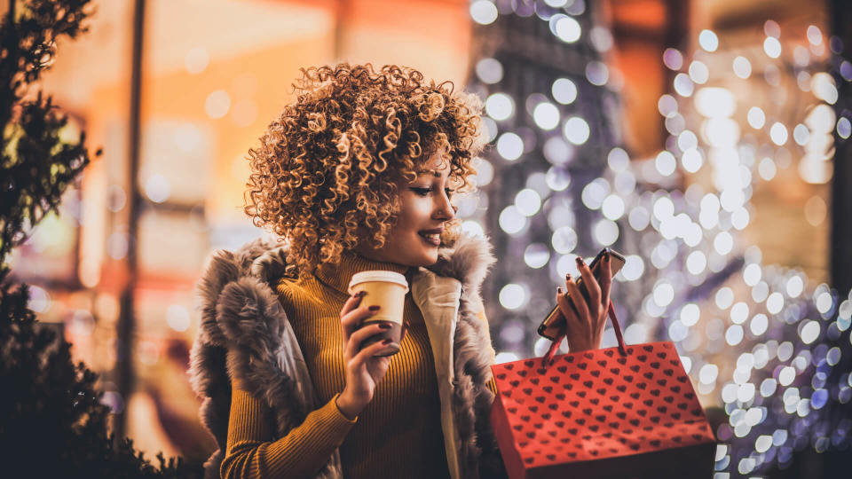 Woman using smartphone and holding shopping bag while standing on the mall background.