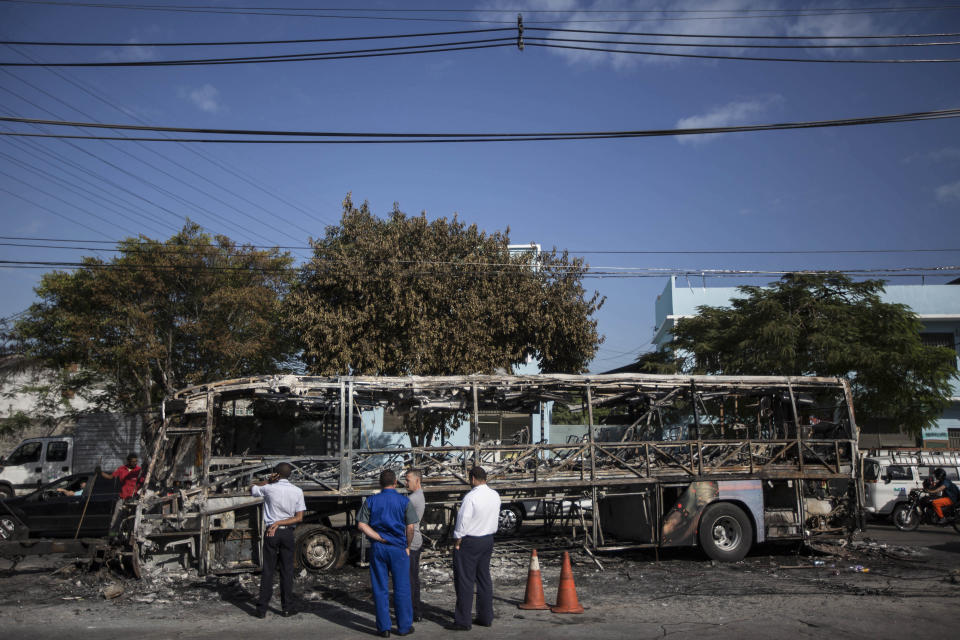 People look at a bus that was set on fire during clashes at the Complexo do Alemao slum complex in Rio de Janeiro, Brazil, Tuesday, April 29, 2014. Brazil police say a gang of suspected drug traffickers ransacked an outpatient clinic and torched four passenger buses during a clash with police hours after three cars were burned near a police outpost. It's the latest unrest to hit Rio's slums just weeks before the country hosts the World Cup. (AP Photo/Felipe Dana)