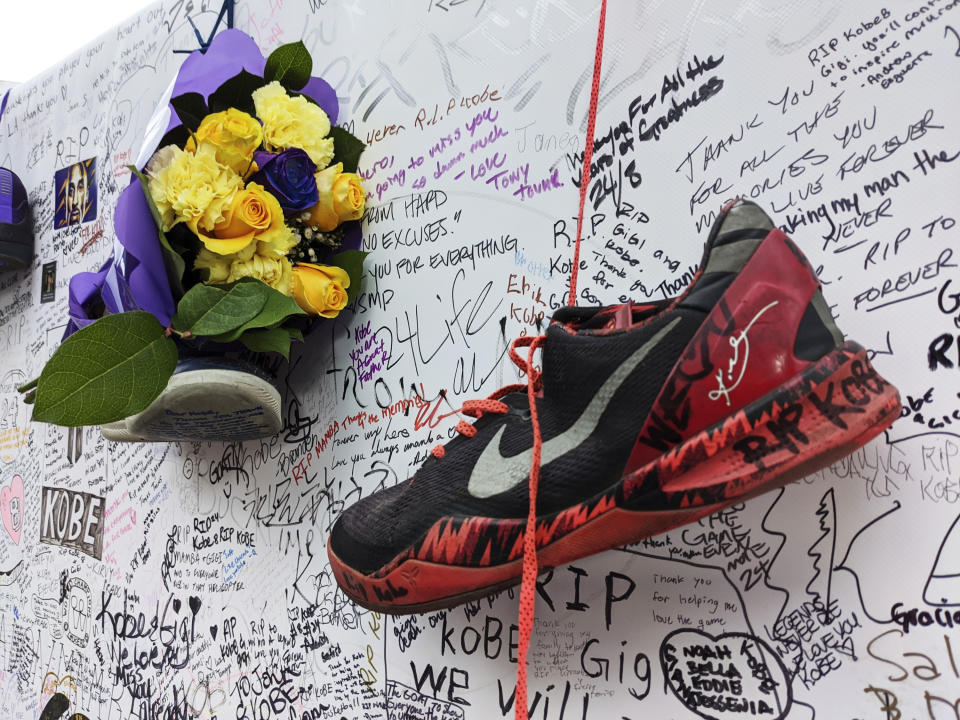 Sneakers and flowers along with messages for NBA star Kobe Bryant are left at a memorial for Bryant while fans gather to pay their respect near Staples Center in Los Angeles Sunday, Feb. 2, 2020. Bryant, the 18-time NBA All-Star who won five championships and became one of the greatest basketball players of his generation during a 20-year career with the Lakers, died in a helicopter crash Sunday, Jan. 26. (AP Photo/Damian Dovarganes)