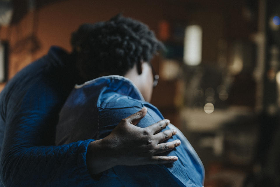 Two people embrace, one with their hand gently resting on the other's back, creating a comforting and intimate moment. Faces are not visible