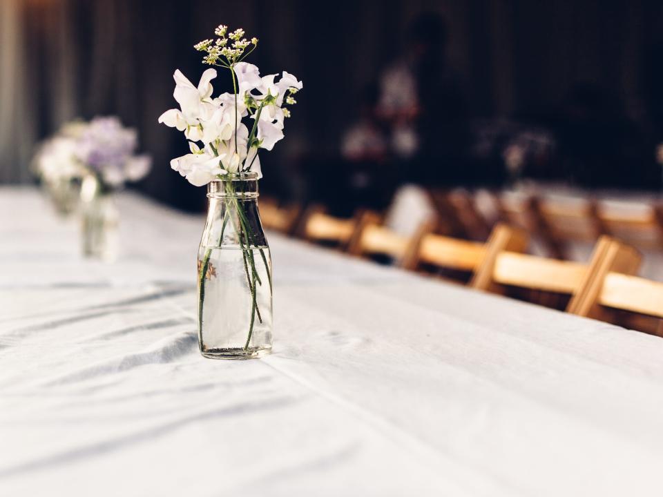 A white table cloth with a small vase of white flowers and wooden chairs