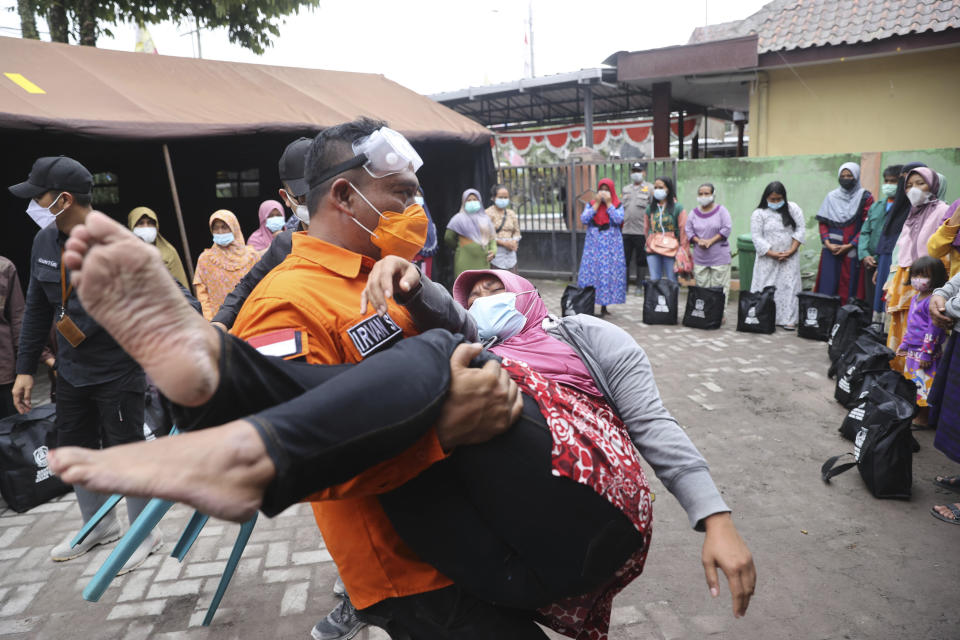 A rescuer holds a woman who fell down in a faint, after seeing her house destroyed by the eruption of Mount Semeru in Lumajang district, East Java province, Indonesia, Sunday, Dec. 5, 2021. The death toll from the eruption of the highest volcano on Indonesia's most populous island of Java has risen by a score of still missing, officials said Sunday as rain continued to lash the area and hamper the search. (AP Photo/Trisnadi)