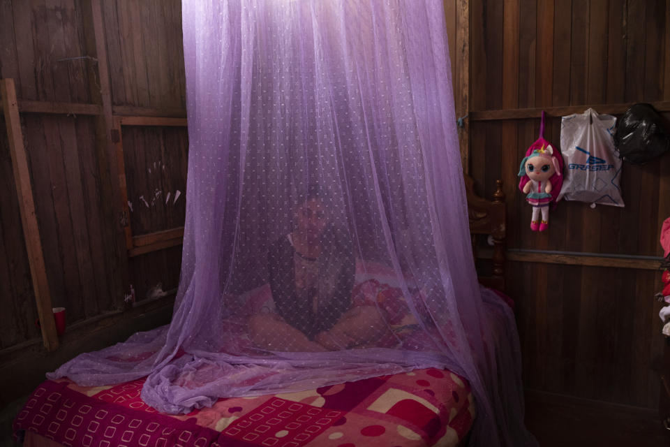 FILE - In this Tuesday, Sept. 29, 2020 file photo, Valentina Esperanza, who is recovering from dengue, sits on her bed protected by mosquito netting as she watches a television program at her home in Pucallpa, in Peru's Ucayali region. Health problems tied to climate change are all getting worse, according to two reports published in the medical journal Lancet on Wednesday, Oct. 20, 2021. The environment in some places is now more conducive to certain mosquitoes that carry malaria and dengue fever. (AP Photo/Rodrigo Abd)