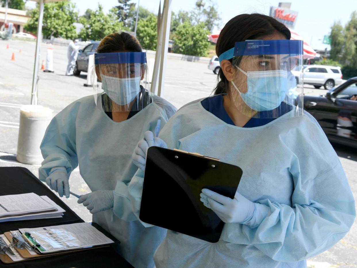 Workers wearing personal protective equipment (PPE) perform drive-up Covid-19 testing administered from a car at Mend Urgent Care testing site for coronavirus at the Westfield Fashion Square on 13 May 2020 in the Sherman Oaks neighbourhood of Los Angeles, California: (2020 Getty Images)