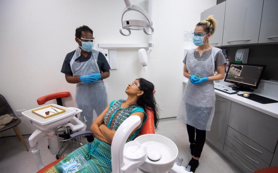 Dentist Dr Roy Woodhoo and Dental Nurse Charlie Coppen wear PPE to examine the first patient through the doors at Woodford Dental Care in north London, as the practice opens up for the first time since the UK went into coronavirus lockdown