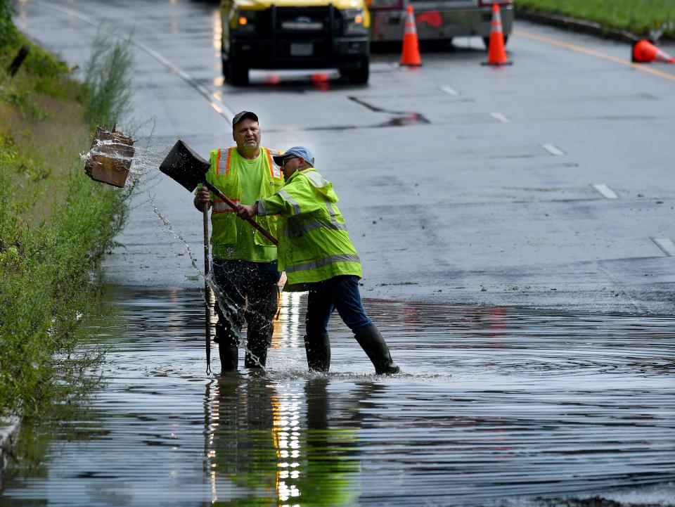 Two Massachusetts Department of Transportation employees work to clear storm drains at the Route 20 and Grafton Street underpass in August 2023. The road was closed in both directions due to flooding from a passing storm