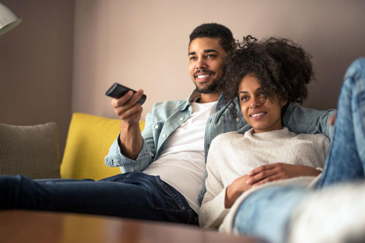 Young couple on couch watching television in living room at home, man is holding the remote