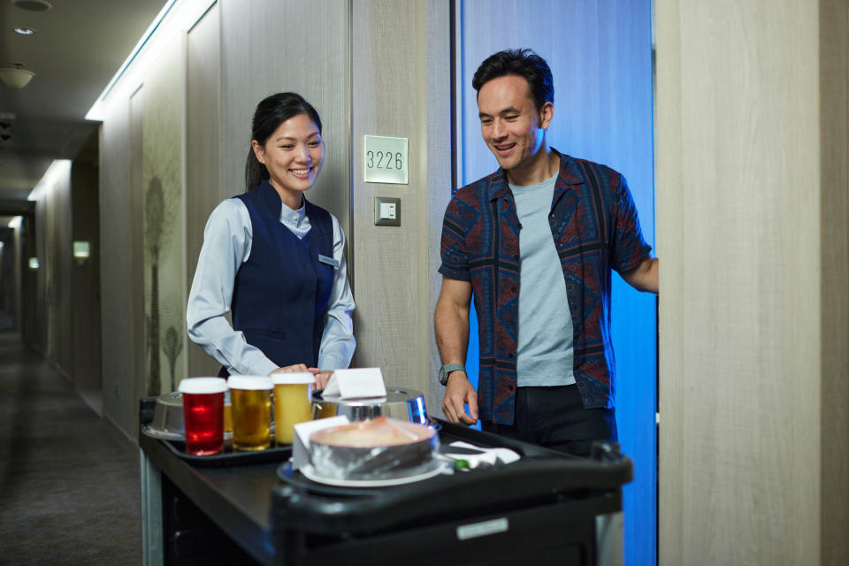 Hotel staff delivering room service to a smiling guest outside a hotel room