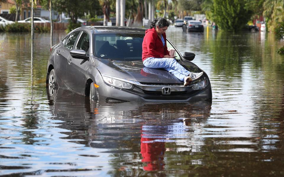 Stephanie Soto sits on the hood of her car after it stalled in floodwaters as she was driving Dec. 23, 2019, in Hollywood, Fla.