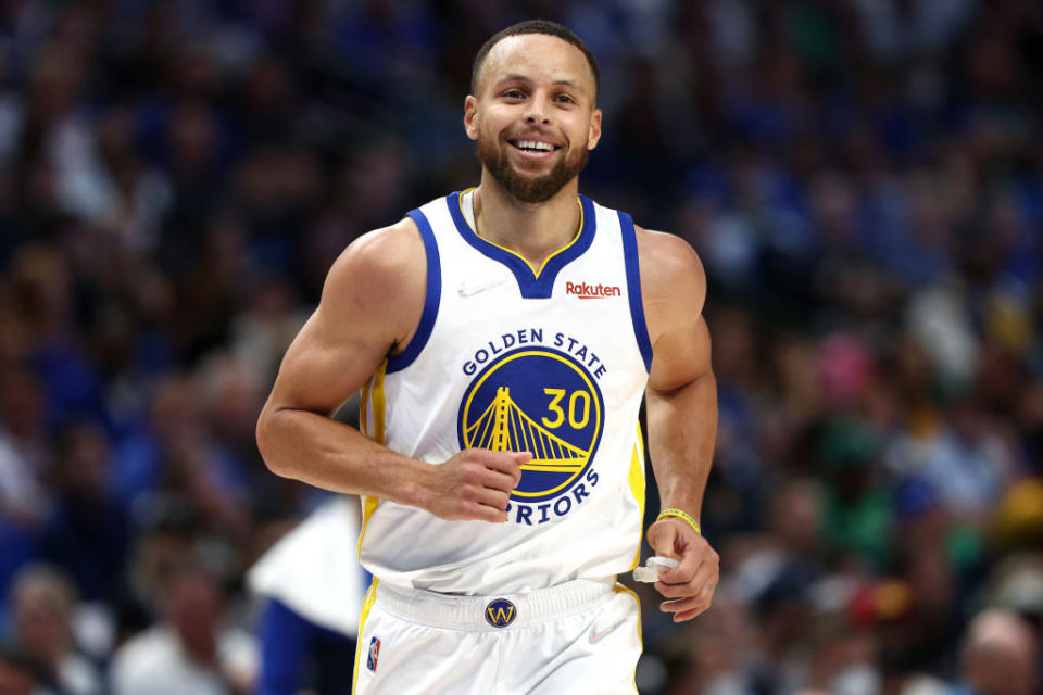 Stephen Curry wearing a Golden State Warriors jersey, mid-action on the basketball court, with a crowd in the blurred background