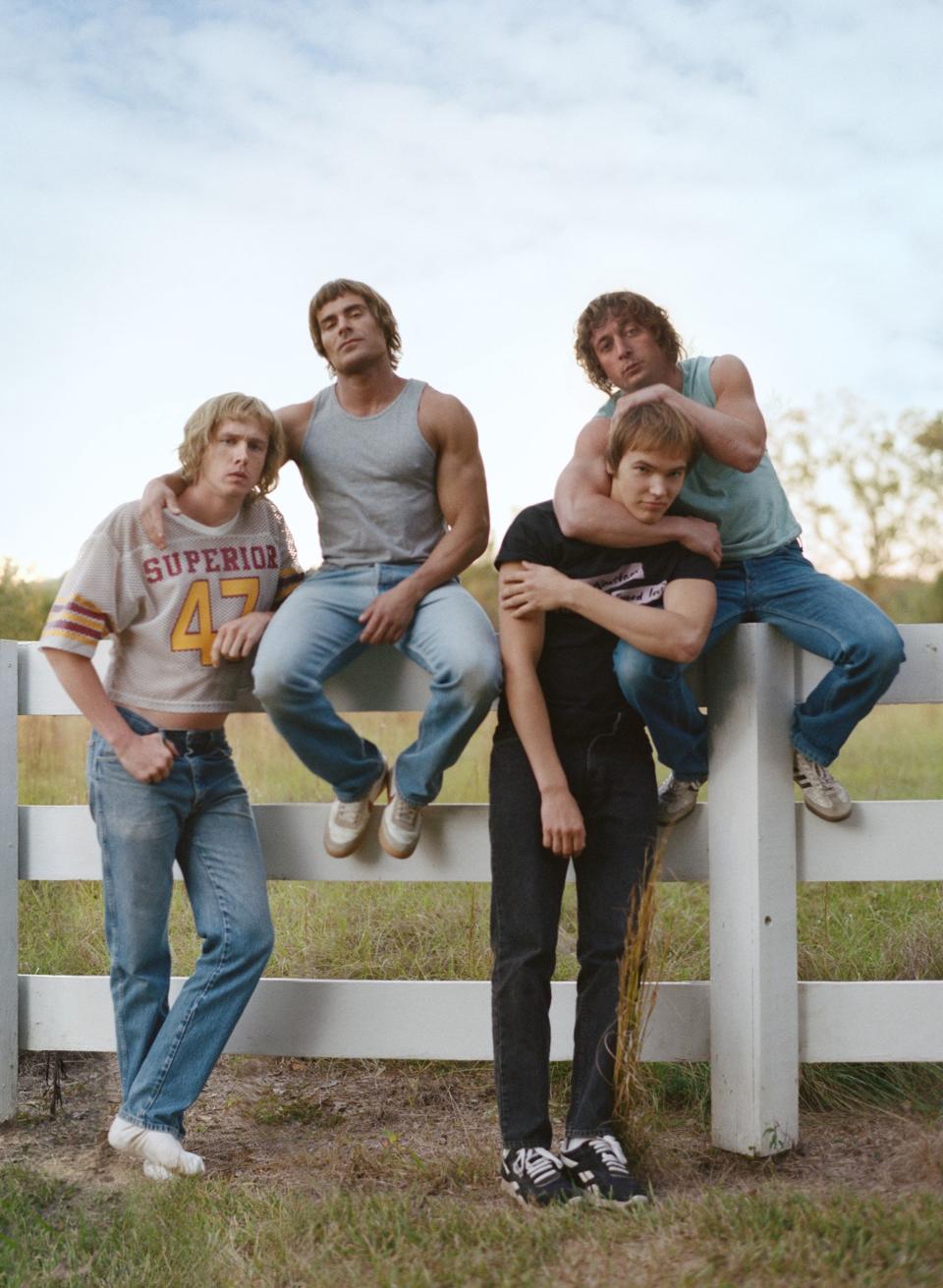 The cast of "The Iron Claw" sitting on ans standing by a fence